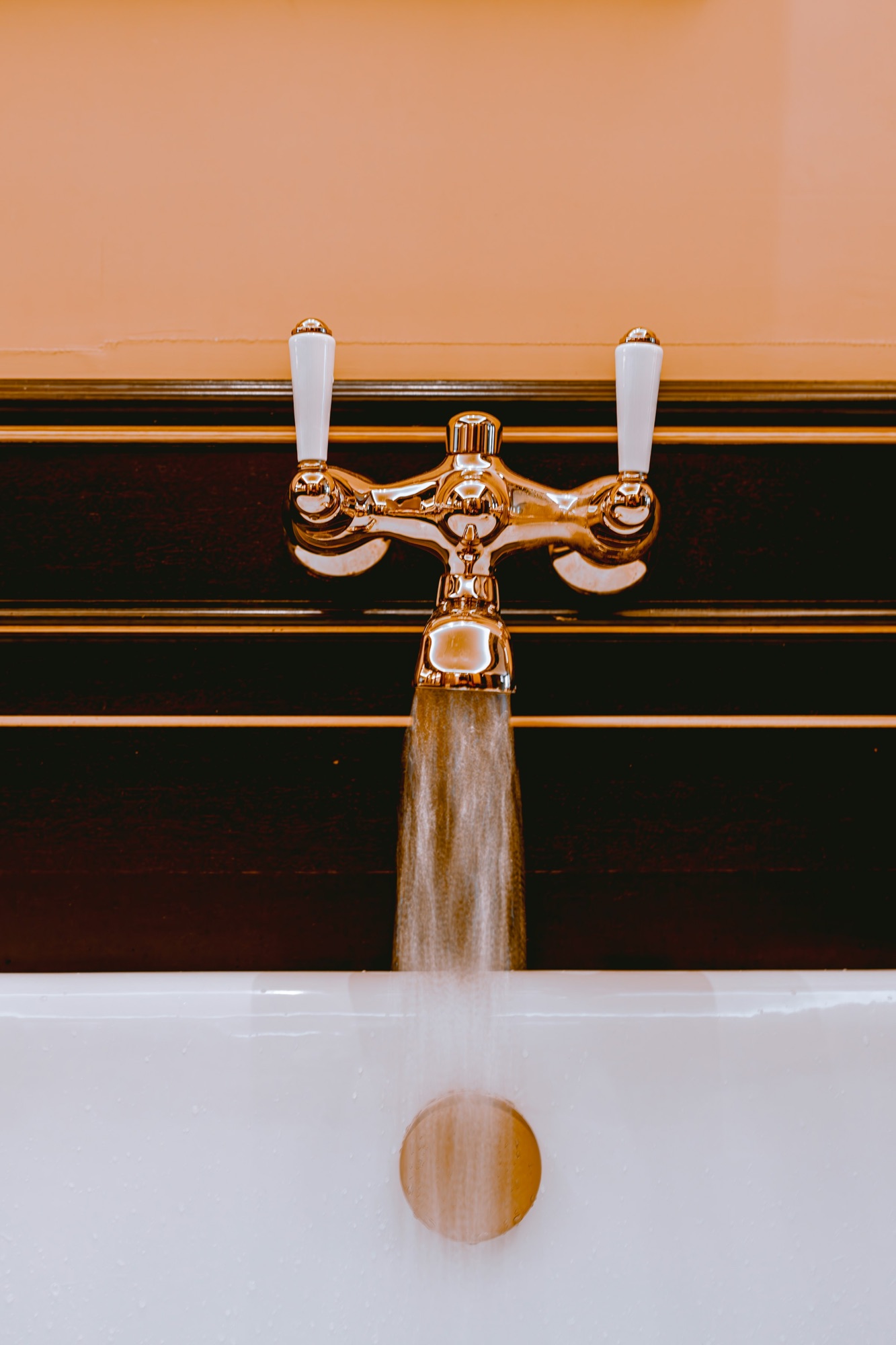 Aged brass crosshead taps running water over a white basin against dark panelling